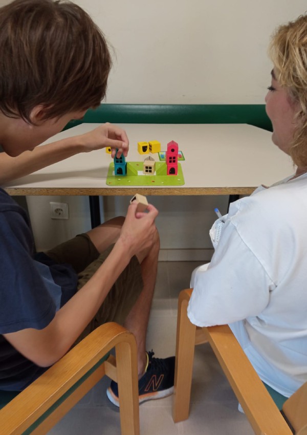 Una persona joven con trastorno del espectro autista organiza unas piezas de colores ante la mirada de una terapeuta